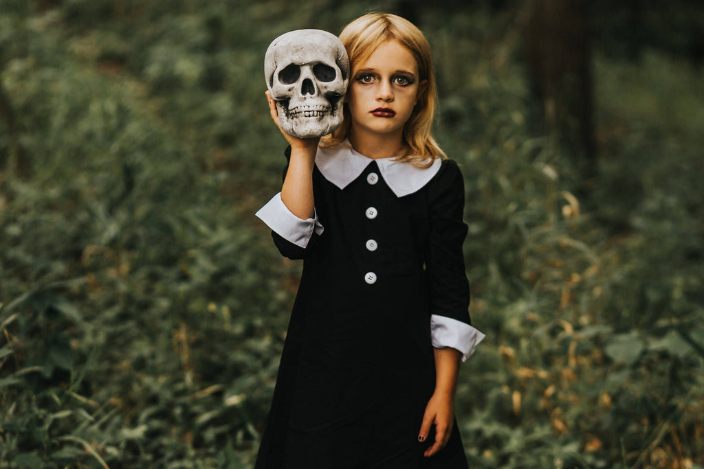 Girl in a black cotton dress with a white Peter Pan collar and cuffed sleeves, holding a skull in a wooded setting.