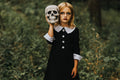 Girl in a black cotton dress with a white Peter Pan collar and cuffed sleeves, holding a skull in a wooded setting.