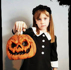 Girl in a black gothic dress with a white Peter Pan collar and cuffs, holding a carved pumpkin for Halloween.