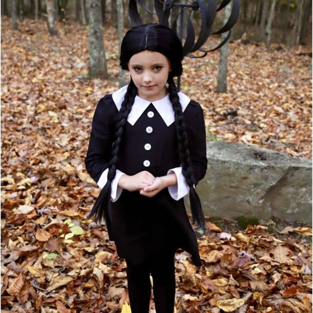 Girl wearing a black cotton dress with a white Peter Pan collar, long sleeves, and button details in an autumn forest setting.