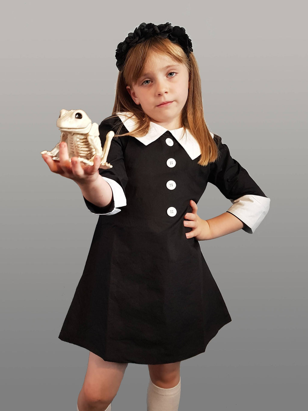 Girl wearing a black cotton dress with a white Peter Pan collar, button front, and cuffed sleeves, holding a skeleton frog.