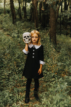 Girl in a black cotton dress with a white Peter Pan collar and cuffs, holding a skull in a forest setting.