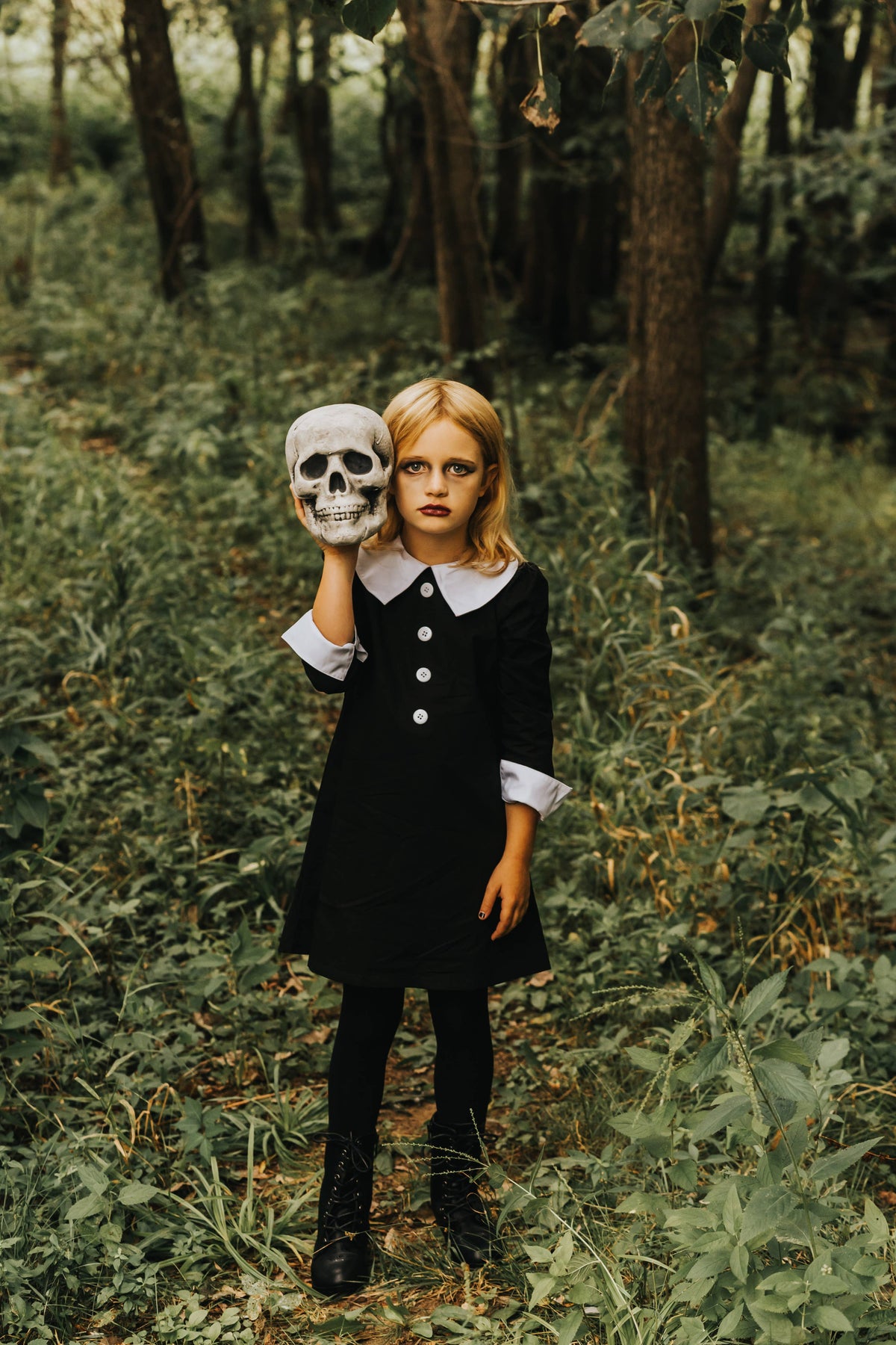 Girl in a black cotton dress with a white Peter Pan collar and cuffs, holding a skull in a forest setting.